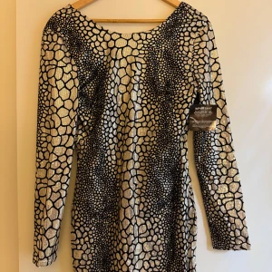 Glittrig kortklänning från NLY One - Säljer en superglittrig kortklänning från NLY One med svart och guldigt mönster. Klänningen har lång ärm, rundad ringning och är täckt av paljetter som verkligen fångar ljuset. Perfekt för dig som vill sticka ut och glänsa på nästa fest!