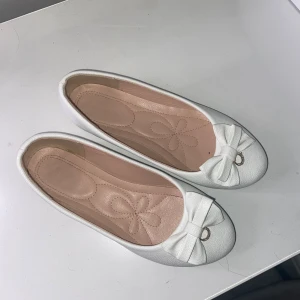 Vita ballerinaskor med rosett  - Söta vita ballerinaskor i storlek 37 med rosett framtill. Rosetten har en liten guldfärgad ring med glittrande stenar som detalj. Endast använd 1 gång 