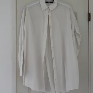 Vit oversized skjorta från Bik Bok - Klassisk vit skjorta från Bik Bok i oversized modell. Skjortan har långa ärmar, knappar hela vägen framtill och en stilren krage. Perfekt för en clean och enkel look. Tillverkad i mjuk bomull som känns skön mot huden.