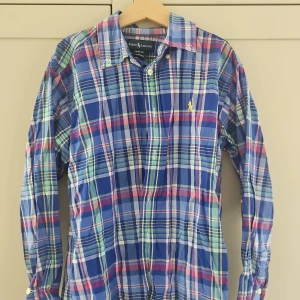 Rutig skjorta från Ralph Lauren M - Färgglad rutig skjorta från Ralph Lauren i bomull. Skjortan har blå, gröna, röda och vita rutor, klassisk krage och knäppning framtill. Ikoniska broderade loggan på bröstet. Perfekt för dig som gillar preppy och stilren look.