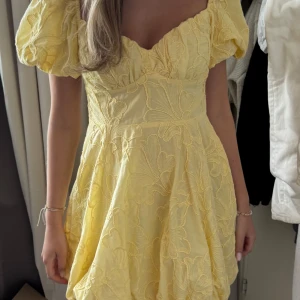 Gul kortklänning med puffärm - Superfin gul kortklänning med puffiga ärmar och v-ringad urringning. Klänningen har broderade blommor över hela tyget och en voluminös kjol som ger en söt och somrig vibe. Perfekt för dig som vill sticka ut med en färgglad och lekfull look. Har kvar prislappen❣️