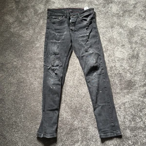Svarta skinny jeans från Dsquared2 - Snygga svarta jeans från Dsquared2 med skinny fit. Jeansen har slitna detaljer, färgstänk och patch med 'Eviction Notice' bak. Klassisk femficksmodell med dragkedja och knapp, samt röd söm på insidan av linningen. Perfekta för dig som gillar en edgy streetstil. Sköna och fina, säljer för jag ej använder dem