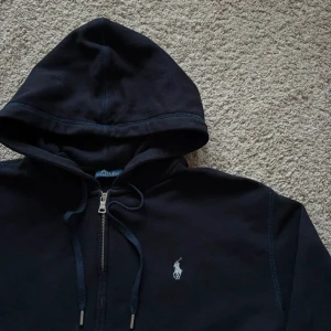 Ralph Lauren Hoodie Navy  - Aviator Navy Ralph Lauren Hoodie med dragkedja, och den ikoniska loggan på vänster bröst broderad i vitt, helt äkta! | STORLEK: S | Nypris: 1900 | Vårt pris (inte hugget i sten): 800 | Skick: 10 / 10, nästan helt oanvänd, inga fläckar, inga märken! Tveka inte med funderingar!