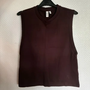 Mörkbrun ärmlös topp & Other Stories - Säljer en stilren mörkbrun ärmlös topp från & Other Stories. Toppen har rund halsringning och är tillverkad i mjuk bomull, perfekt för en clean och avslappnad look. Passar lika bra till jeans som kjol. Ej använd!