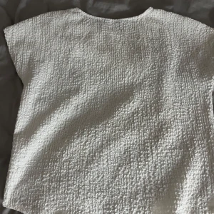 Vit strukturerad blus  - Säljer en vit blus  med korta ärmar och rund halsringning. Tyget är strukturerat och har en lätt krinklad känsla som ger toppen en cool och modern look. Perfekt att styla med jeans eller kjol för en fräsch outfit. Andvänd få tal gånger. Pris kan diskuteras💓💓💓