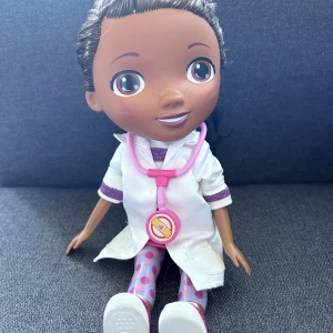 Vit rock med lila detaljer till docka - De är en docktormcstuffin som är lite andvänd för många år sen. Kan styla om håret om de är så, väldigt fin docka😊 