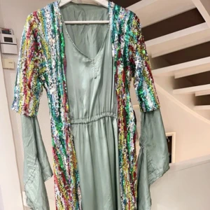 Glittrig ljusblå kurdisk klänning med paljetter - Ljusblå kurdisk klänning i tyg med färgglada paljetter i ränder över hela klänningen. Klänningen har v-ringning, vida ärmar och ett flowy fall. Perfekt för dig som vill sticka ut med färg och glitter. Storlekarna S, M och L✨