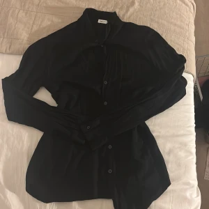 Svart skjorta från Filippa K - Stilren svart skjorta från Filippa K i ett tunt och mjukt material. Klassisk krage, långärmad och knäppning framtill. Perfekt för dig som gillar minimalistisk och clean stil.