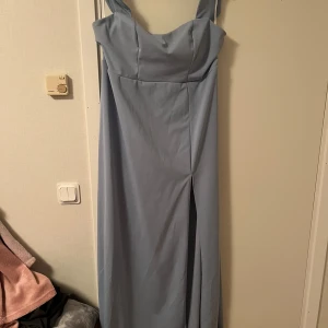 Ljusblå långklänning med slits - Snygg ljusblå långklänning med breda axelband och markerad byst. Klänningen har en elegant slits framtill och en diskret dragkedja i ryggen. Perfekt för dig som vill ha en stilren och modern look. Katt finns i hemmet