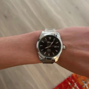 Svart och silver klocka från Doventi  - Stilren klocka från Doventi med svart urtavla och datumvisning. Armbandet är i silverfärgat metall och klockan har tydliga indexmarkeringar. Klassisk design som passar till många olika outfits.