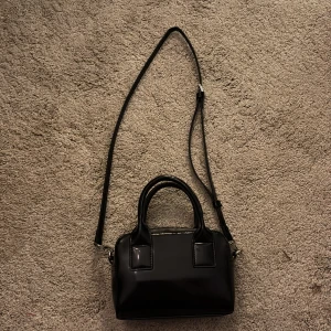 Liten axelväska  - En liten axelväska, man kan ta bort dom långa banden så de blir en handväska, köp på Åhléns för 300. Andvänd en gång. 