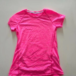 Rosa sport-t-shirt från H&M - Snygg rosa sport-t-shirt från H&M med korta ärmar och rund hals. Tillverkad i ett lätt och stretchigt material som passar perfekt för träning. T-shirten har en fräsch, neonrosa färg och diskret mönster i tyget för en cool look.