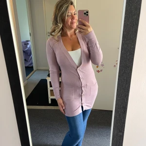 Ljuslila kofta med knappar - Lång, ljuslila kofta med v-ringning och knappar framtill. Koftan har två fickor och är tillverkad i en mjuk mix av kashmir, ull, bomull, polyamid och elastan. Perfekt att slänga över en topp för en chill look.Oanvänd.Storlek som är på etiketten är L-XL men enligt mig passar bättre från S till L