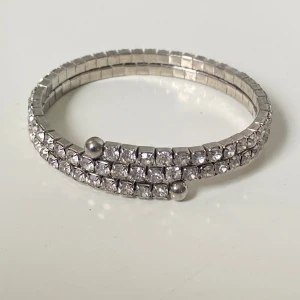 Glittrigt silverfärgat armband - Snyggt armband i silverfärg med två rader gnistrande stenar som ger en riktigt glittrig look. Armbandet är elastiskt och har små silverkulor som detalj. Perfekt för dig som vill sticka ut med lite extra bling.