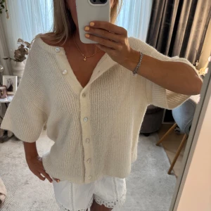 Vit stickad kofta från Gina Tricot - Superfin vit stickad kofta från Gina Tricot med korta ärmar. Koftan har ribbad struktur, knappar framtill och en loose fit som ger en chill vibe. Perfekt att slänga över ett linne eller t-shirt för en avslappnad look.