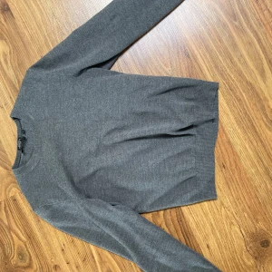 Grå merinoulltröja från BOSS - Snygg grå tröja från BOSS i mjuk och exklusiv merinoull. Regular fit med rund halsringning och diskret broderad logga på bröstet. Perfekt för dig som gillar stilrena och klassiska plagg med premiumkänsla. Ska tilläggas att den har blivit lite lätt krympt i tvätten så den passar s/xs