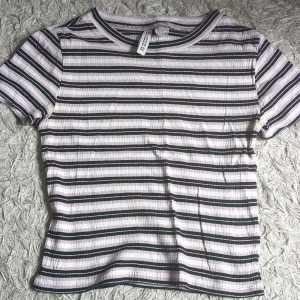 Baby tee - Superfin kortärmad topp från HM med smala svarta, vita och lila ränder. Ribbad struktur och klassisk rund halsringning. Perfekt att matcha med jeans eller kjol för en chill look.