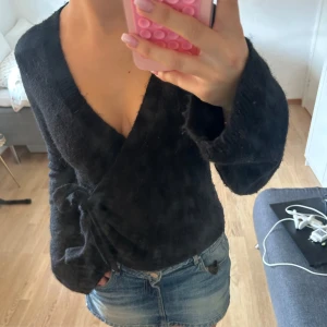 Svart omlottkofta  - Mysig svart omlottkofta med knytband i midjan och djup v-ringning. Koftan är stickad och har långa ärmar, perfekt för lager-på-lager och chill outfits. Passar snyggt till jeans eller kjol för en avslappnad men ändå stilren look. Kommer inte till användning hos mig och därför ja säljer 💕