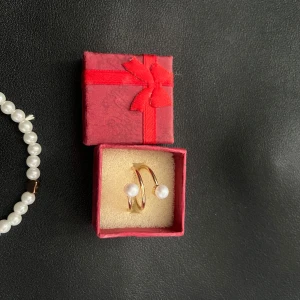 Guldring och pärlarmband - Säljer ett snyggt armband med vita pärlor och en guldig ring med två pärlor. Ringen har en öppen design och armbandet är elastiskt med en liten guldig detalj. Perfekt för dig som gillar klassiska smycken med en modern twist.