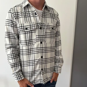 Vit och svart rutig overshirt från H&M - Säljer nu min snygga overshirt från H&M i vitt med svart rutigt mönster. Långärmad med normal passform. Passar perfekt över en t-shirt 