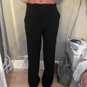 Svarta kostymbyxor med raka ben - Snygga svarta kostymbyxor med hög midja och raka ben. Byxorna har diskreta fickor fram och bak, samt hällor för bälte. Perfekta för en clean och stilren look. Materialet känns mjukt och följsamt.
