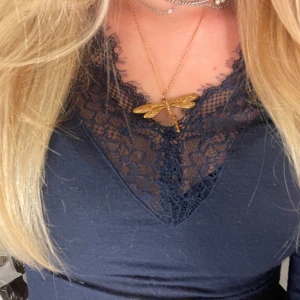 Guldigt halsband med trollslända - Unikt halsband med en stor trollslända som hänge i guldtonad metall. Kedjan är tunn och elegant, och trollsländan har fina detaljerade mönster på vingarna. Perfekt statement piece för dig som vill sticka ut med din stil.