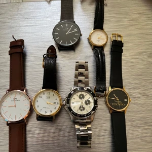Samling av sju klockor - Säljer en samling av sju klockor med olika stilar och material. Inkluderar klockor med läderband i brunt och svart, en med metallarmband i silver, samt en med svart meshband. Urtavlorna varierar i färg från vit till svart och guld. Perfekt för den som vill ha variation i sin klocksamling. Vet ej funktion i någon av dem och alla behöver byta batteri!