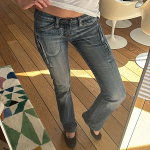 Blå jeans med dragkedjedetaljer - Snygga blå jeans med dragkedjor på sidorna och en klassisk femficksdesign. De har en låg midja och en straight passform som ger en avslappnad look. Perfekta för en cool och casual stil.