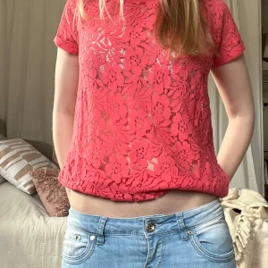 Rosa spetsblus - Säljer en snygg rosa spetsblus med korta ärmar. Perfekt för att lägga till en touch av elegans till din outfit. Blusen har ett blommigt mönster och är lätt transparent, vilket ger en chic look.