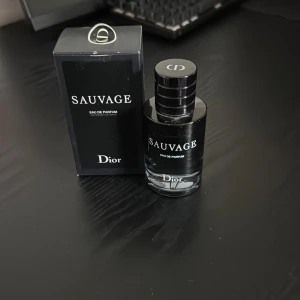 Sauvage Eau de Parfum från Dior - Säljer en flaska Sauvage Eau de Parfum från Dior. Flaskan har en elegant design med en mörk tonad glasflaska och svart lock. Perfekt för den som söker en sofistikerad och maskulin doft.