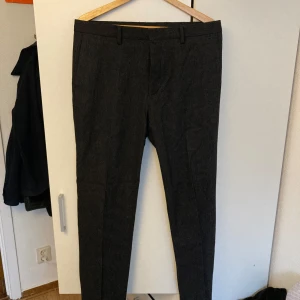 Grå kostymbyxor i flanell - Snygga grå kostymbyxor från Riley i slim fit. Mörkgrå i ett flannelmaterial, storlek 48 och i mycket bra skick.