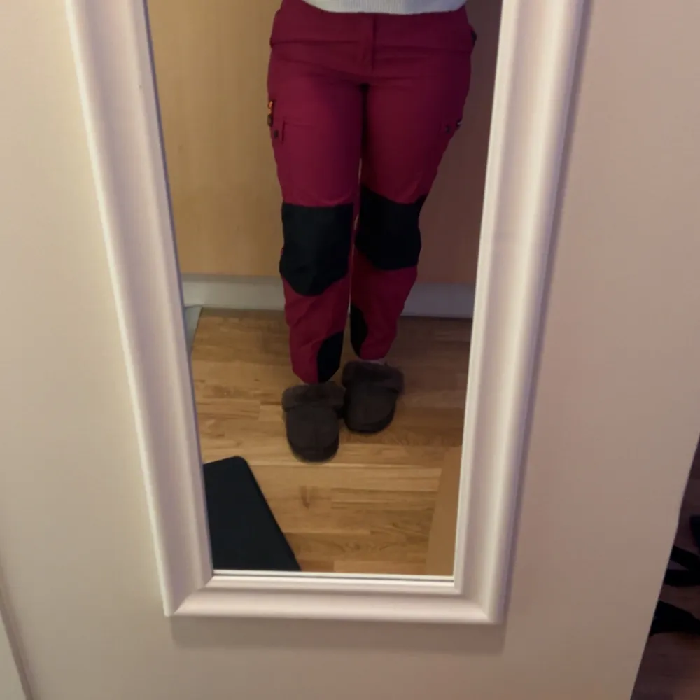 Snygga och funktionella friluftsbyxor från Pinewood i rosa och svart. Byxorna har flera praktiska fickor med knappar och dragkedjor, perfekt för utomhusaktiviteter. De är designade för att vara slitstarka och bekväma, med förstärkningar på knän och bakdel.. Farkut & Housut.