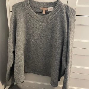 Grå stickad tröja från H&M - Säljer en mysig grå stickad tröja från H&M. Perfekt för kyliga dagar med sin mjuka och bekväma passform. Tröjan har långa ärmar och en klassisk rund halsringning.