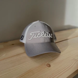 Titleist Keps - Snygg keps från Titleist i grått och vitt med broderad logga framtill. Kepsen har en justerbar baksida i meshmaterial för extra ventilation. Perfekt för golf eller andra utomhusaktiviteter nu till sommarn. Är öppen för alla frågor! 😁😁