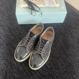  Lanvin - Snygga grå sneakers från Lanvin med en glansig tå och snörning. Har box och kvitto från nk. Perfekta för en trendig look.