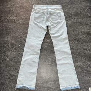 Långa jeans från pull&bear - Säljer ett par ljusblå jeans från Pull&Bear med en klassisk femficksdesign och knappgylf. Jeansen har en rak passform och råa kanter vid bensluten för en trendig look.