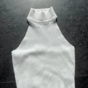 Vit ribbad polotopp - Snygg vit ribbad polotopp med hög krage. Toppen är ärmlös och har en stilren design som passar perfekt för lager-på-lager eller som den är. Perfekt för en chic och minimalistisk look.