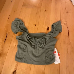 Grön ribbad topp från Cider - Säljer en söt grön ribbad topp från Cider med korta ärmar och knytning framtill. Toppen har en croppad passform och volangdetaljer vid ärmarna. Perfekt för en somrig look! 🌿Den är aldrig använd!