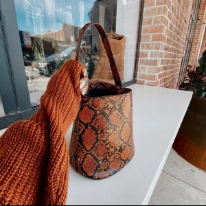 Brun axelväska med ormmönster - Snygg brun axelväska med ormmönster från Nasty Gal. Väskan har en enkel design med ett handtag och en rymlig insida. Perfekt för att ge din outfit en trendig touch.