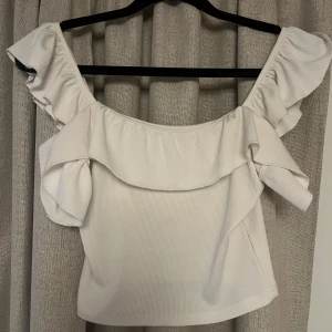 Vit ribbad topp med volang - Säljer en söt vit ribbad topp med volangdetaljer. Perfekt för sommarens alla tillfällen. 🕊️
