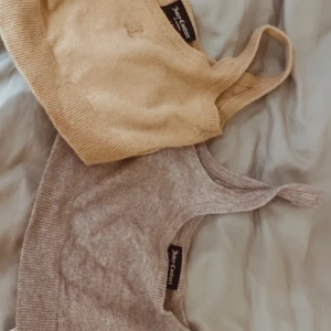 Beige och grå croppad linnetopp från Juicy Couture - Två snygga croppade linnen från Juicy Couture i beige och grått. De är ribbade och har breda axelband, perfekta för en stilren look. Passar bra till både jeans och kjol.