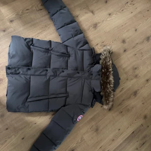 Canada goose jacka  - Säljer en svart dunjacka från Canada Goose med pälsdetalj på huvan. Jackan har en klassisk pufferdesign med långa ärmar och flera praktiska fickor. Perfekt för kalla vinterdagar. Använd 1 gång