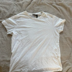 Vit t-shirt från ASOS DESIGN - Säljer en klassisk vit t-shirt från ASOS DESIGN. Den har en rund halsringning och korta ärmar, perfekt för en enkel och stilren look. Tillverkad i mjukt material för en bekväm passform. Perfekt basplagg i garderoben!