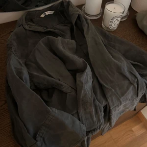 Grå skjorta från Zara - Säljer en grå skjorta från Zara. Den har en avslappnad passform med något kortare ärmar än normalt och knappar framtill. Färgen gör sig inte riktigt rättvis på dem sista två bilderna pga ljuset, den är mörkgrå som syns på dem första bilderna och inte brun 🤍Endast använd en gång