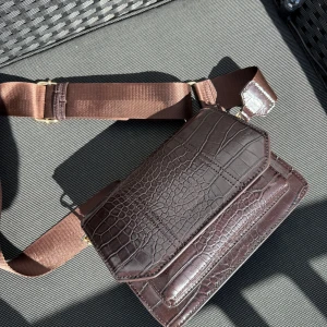 Brun axelväska från NAKD - Snygg brun axelväska i syntet med krokodilmönster. Från NAKD, helt ny, Väskan har en justerbar axelrem och flera fack med dragkedja och tryckknapp för enkel organisering. Perfekt för att hålla dina saker säkra och stiliga.