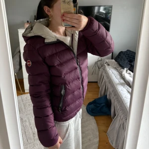 Vinröd dunjacka från Colmar - Säljer en snygg vinröd dunjacka från Colmar med dragkedja och två praktiska fickor. Jackan har en ljus insida och är perfekt för kyligare dagar. Den är långärmad och har en stilren design som passar till mycket. Perfekt för dig som vill hålla värmen med stil! 💜