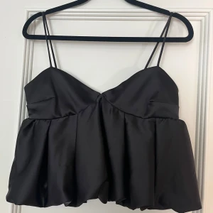 Svart satinlinne med smala axelband - Elegant svart linne i satin med smala axelband och en luftig passform. Toppen har en smockad rygg för extra komfort och stil. Passar bra på mig med lite större byst som vanligtvis har XS/S i toppar!