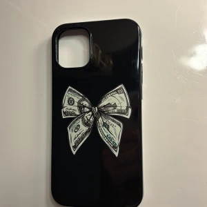 Svart mobilskal med sedel rosett  - Snyggt svart mobilskal med ett unikt motiv av en rosett gjord av dollarsedlar. Perfekt för att ge din telefon en stilfull och iögonfallande look. Skalet är slimmat och skyddar din mobil effektivt.