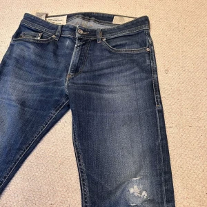 Blå jeans med slitningar - Snygga blå jeans med en tight passform och slitningar på framsidan. De har en klassisk femficksdesign och knappar i midjan. Perfekta för en avslappnad stil.