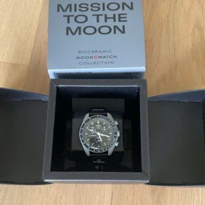 Omega x Swatch Speedmaster MoonSwatch - Säljer en Omega x Swatch Speedmaster MoonSwatch från Bioceramic MoonSwatch Collection. Klockan har en svart urtavla med vita detaljer och en svart armband. Den kommer i originalförpackning med extra armband.